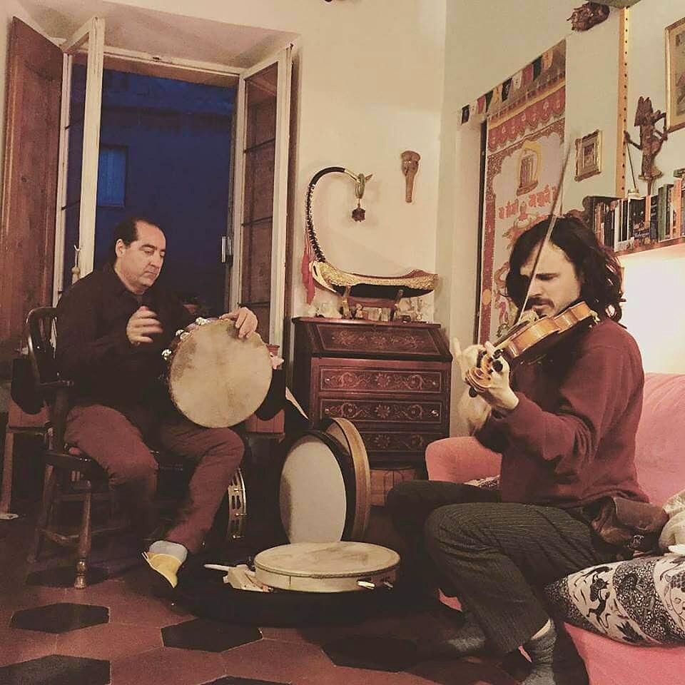 Accordi di Pace rehearsal. Two musicians, one playing frame drum, one playing violin, in an intimate Roman interior.