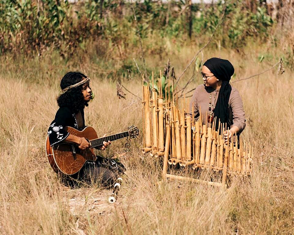 Piccoli Grandi Concerti. Two musicians playing guitar and bamboo percussion in an open field.