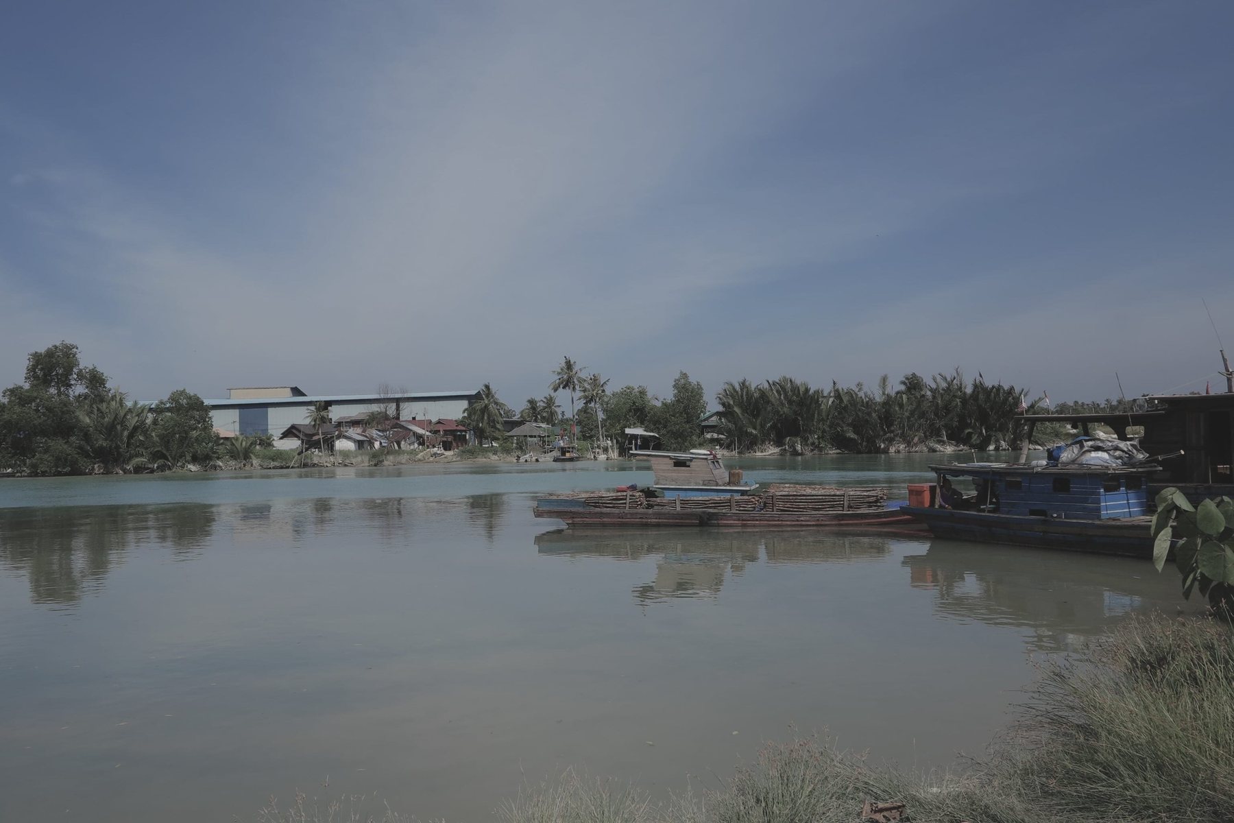 Contemporary photograph of the Batu Pahat River in Malaysia, showing the water and banks under clear sky.