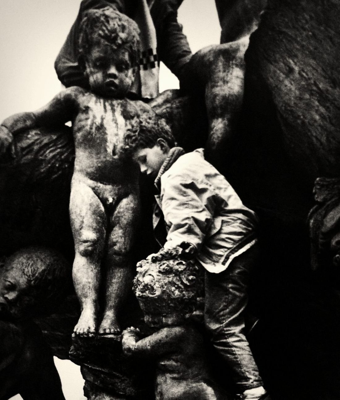 A boy climbing among the bronze children of a monument.