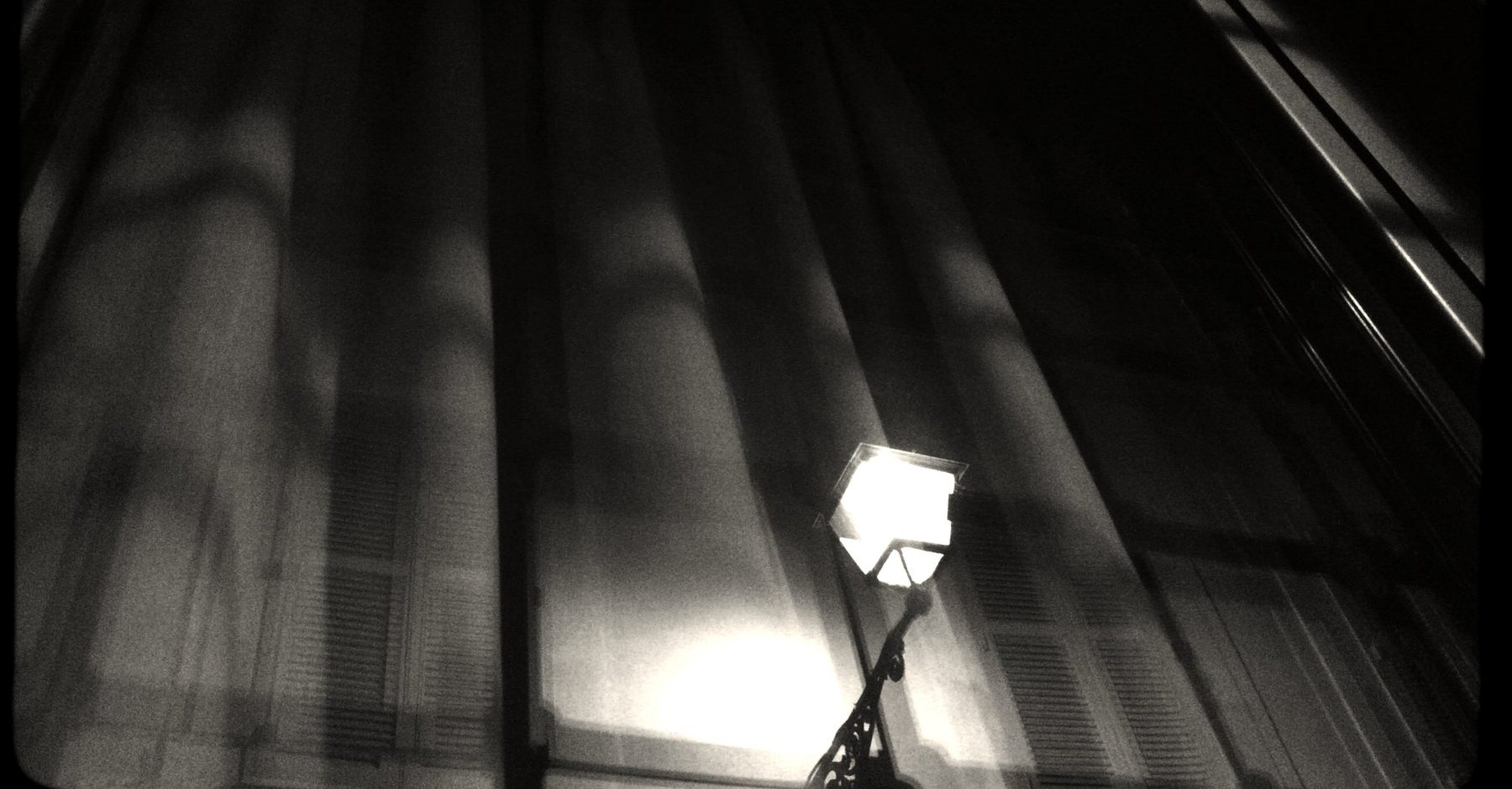A street lamp burning against a blurred façade at night.