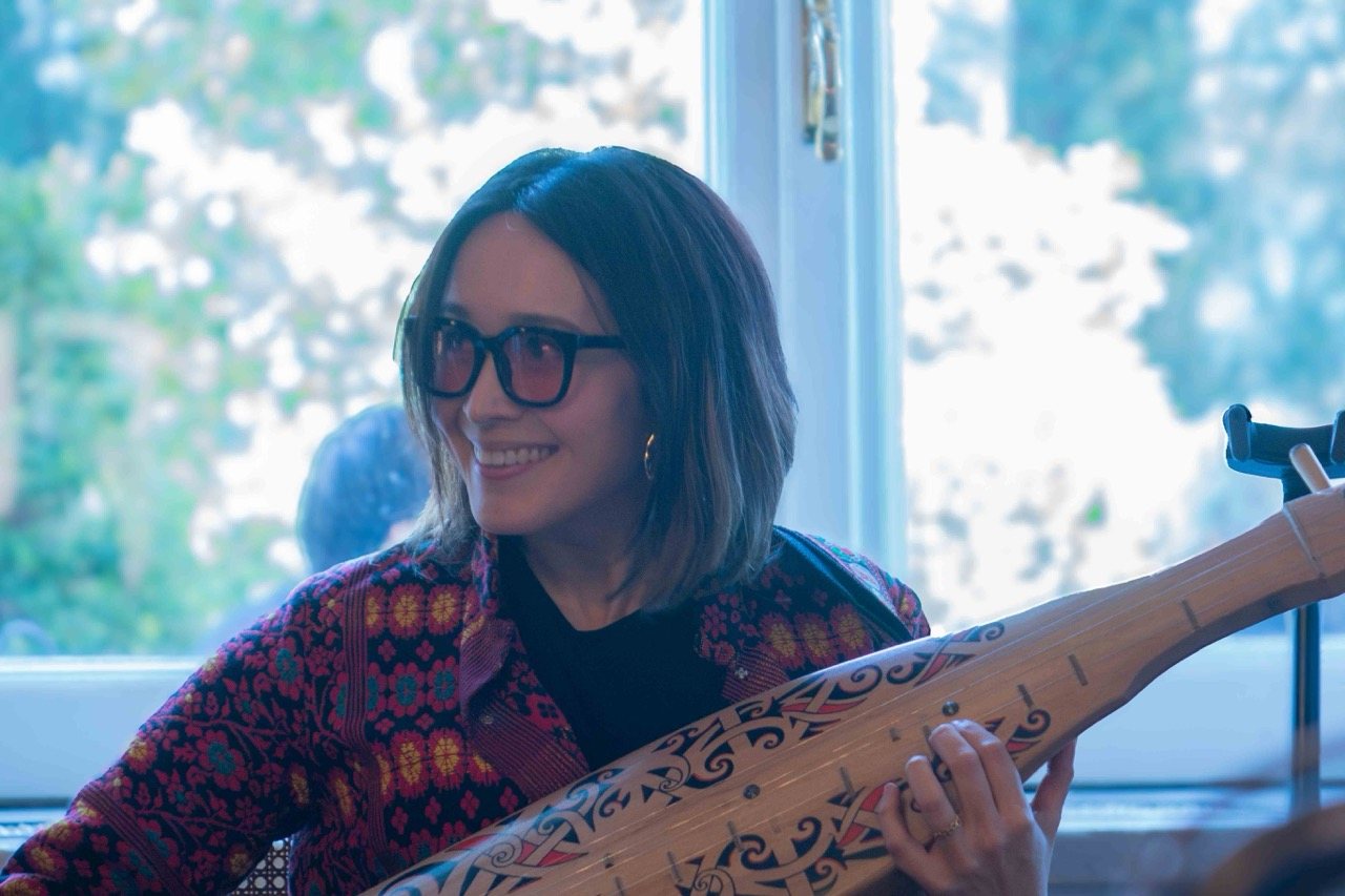 Close-up of a woman playing the sape, a Bornean lute with carved spiral patterns along its neck.