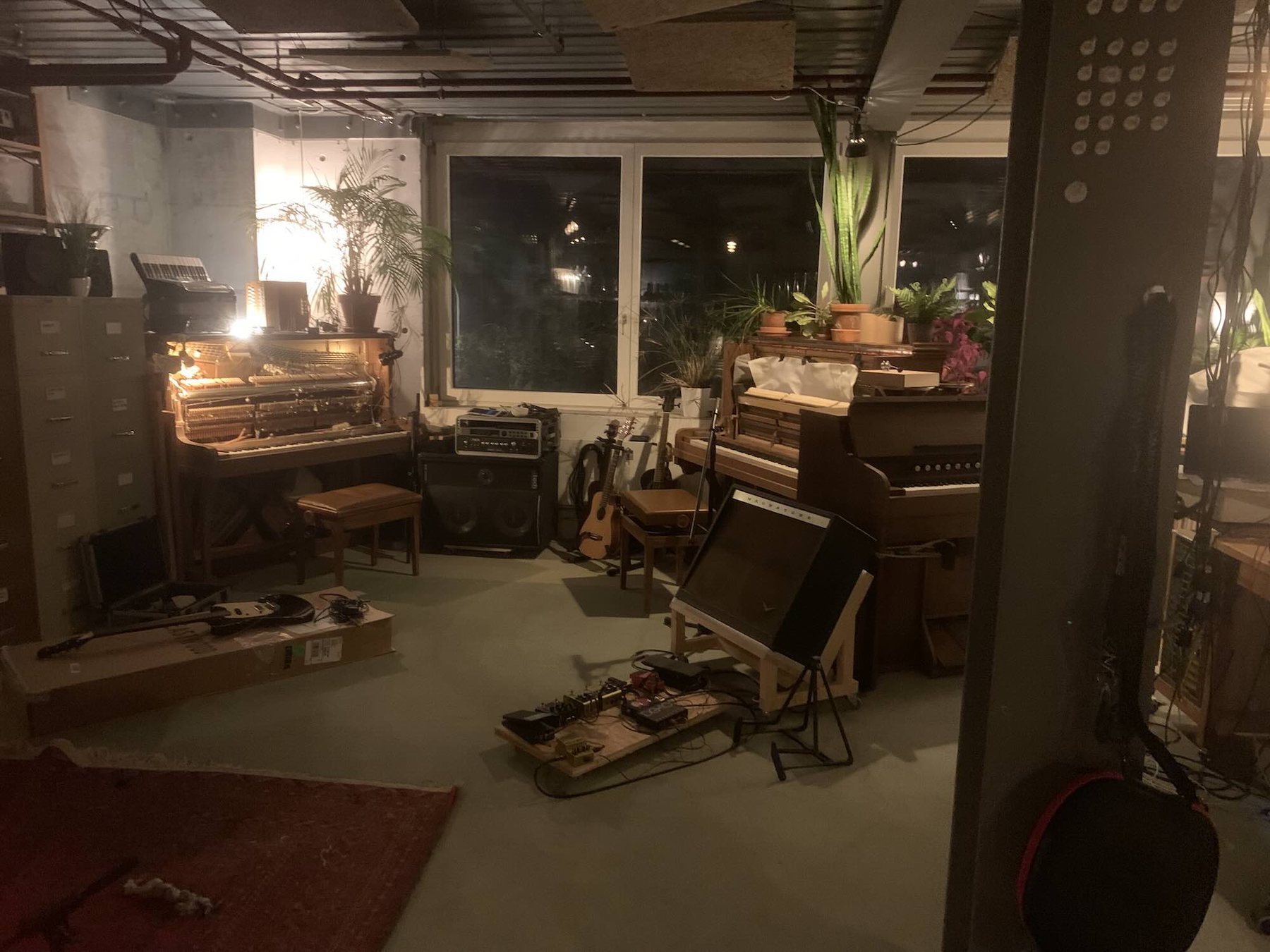 A studio room with several pianos, an accordion, and guitars arranged among plants and recording equipment.