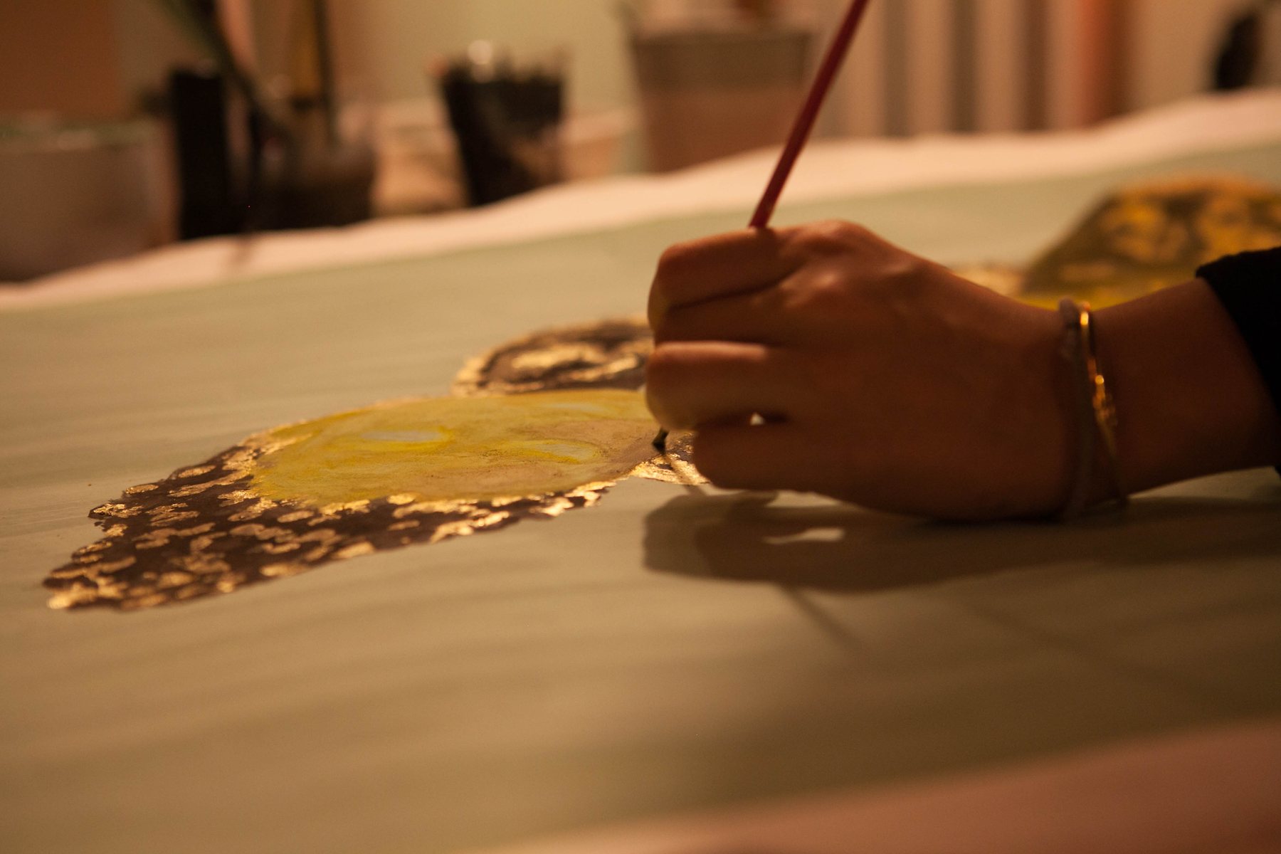 Close-up of a hand holding a fine brush, applying gold leaf to a painted surface.