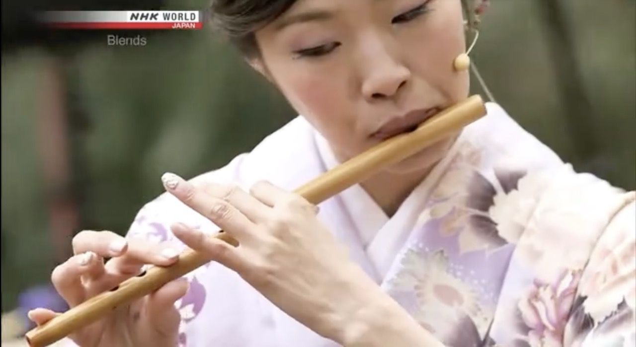 Sarah Akiyoshi playing shinobue in an NHK World Blends performance, outdoors, in white kimono.