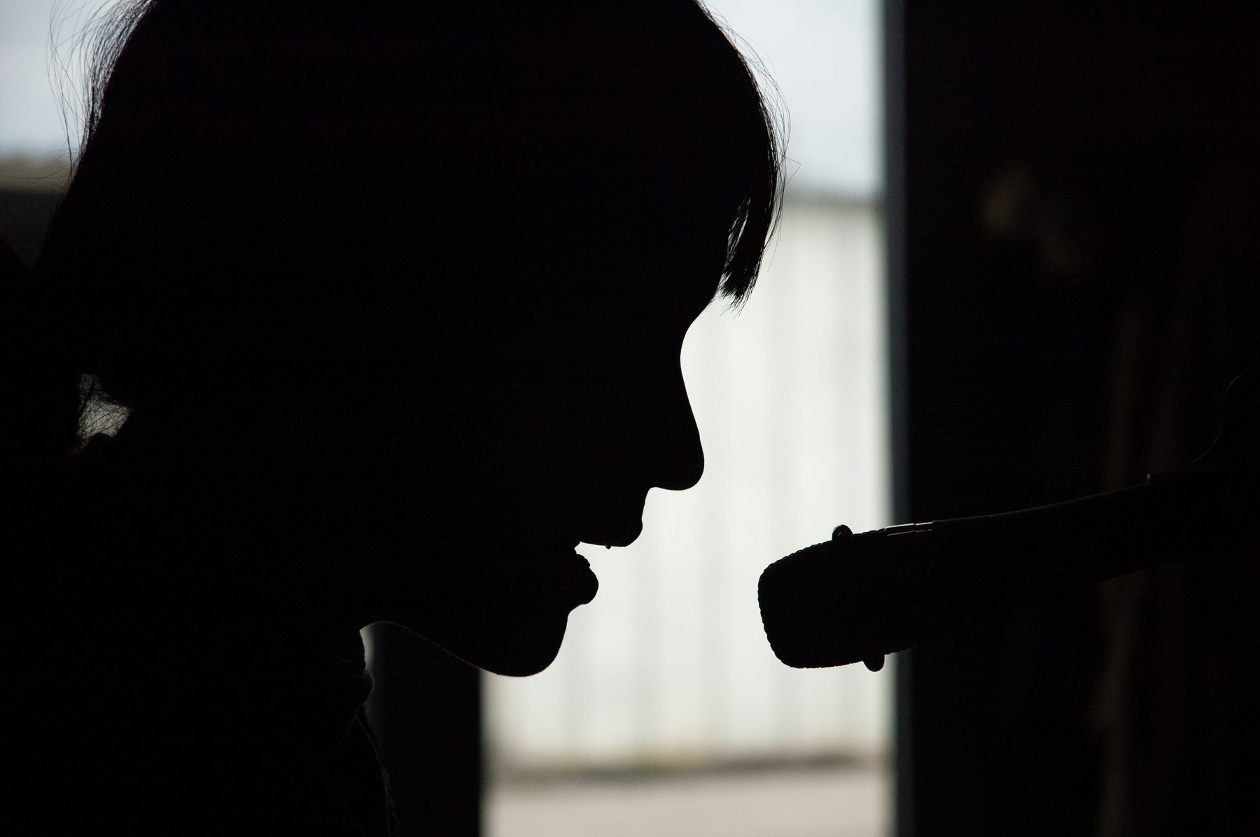 Silhouette profile of a figure playing a wind instrument in near-darkness, strong backlight, the instrument extended forward.