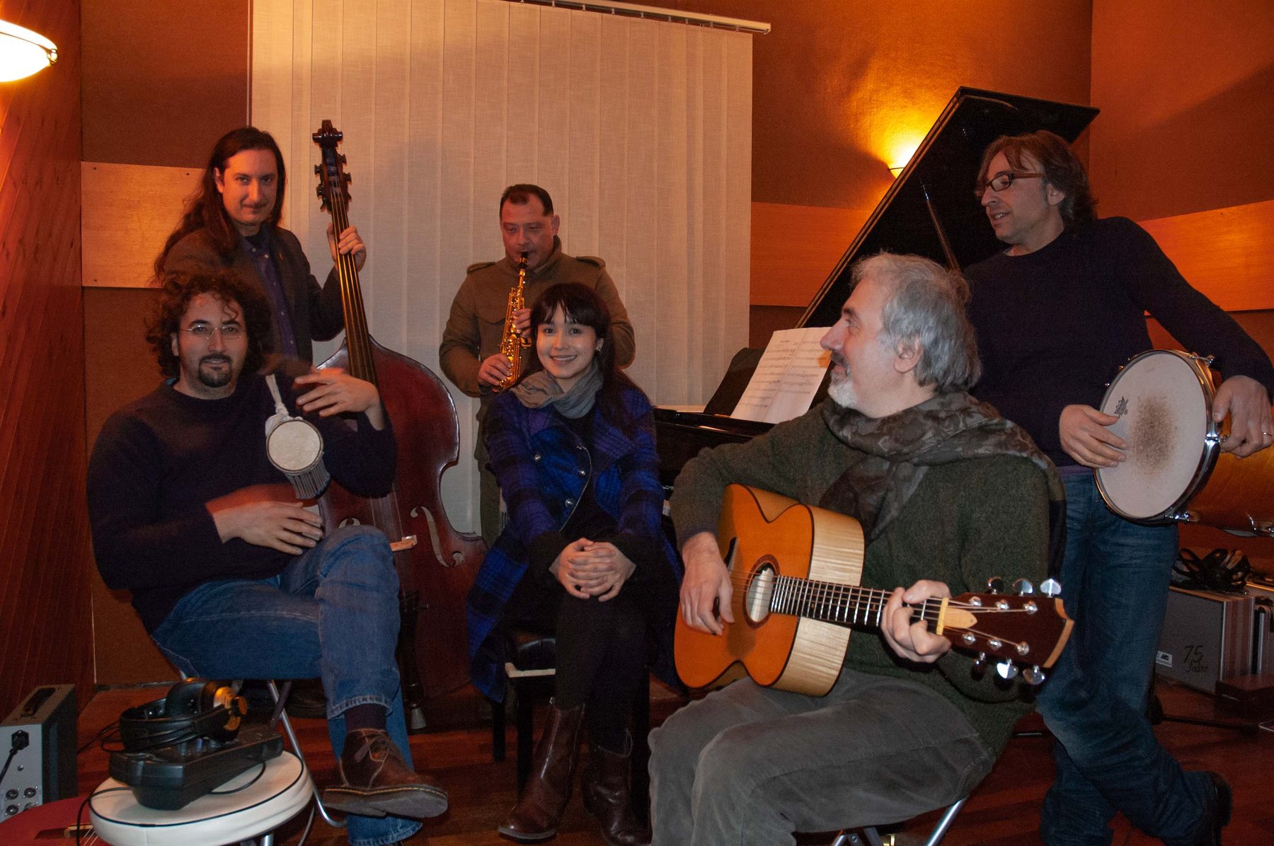 The ensemble mid-session in the studio, the saxophone player playing, others listening and playing together, scores on stands, warm amber studio light.