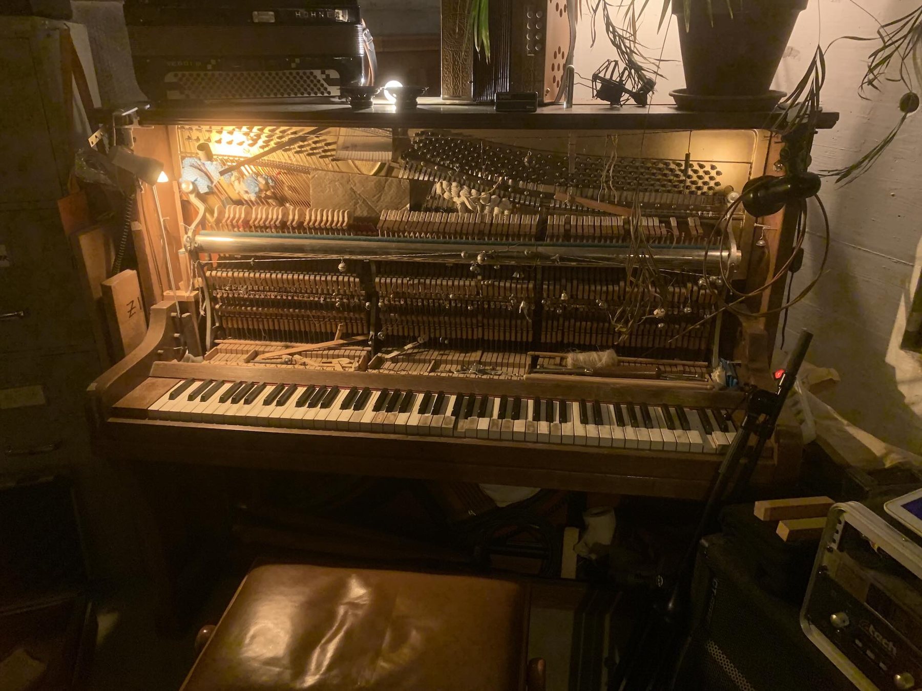 A prepared upright piano viewed from the front, hammers and dampers exposed, tools resting inside the open mechanism.