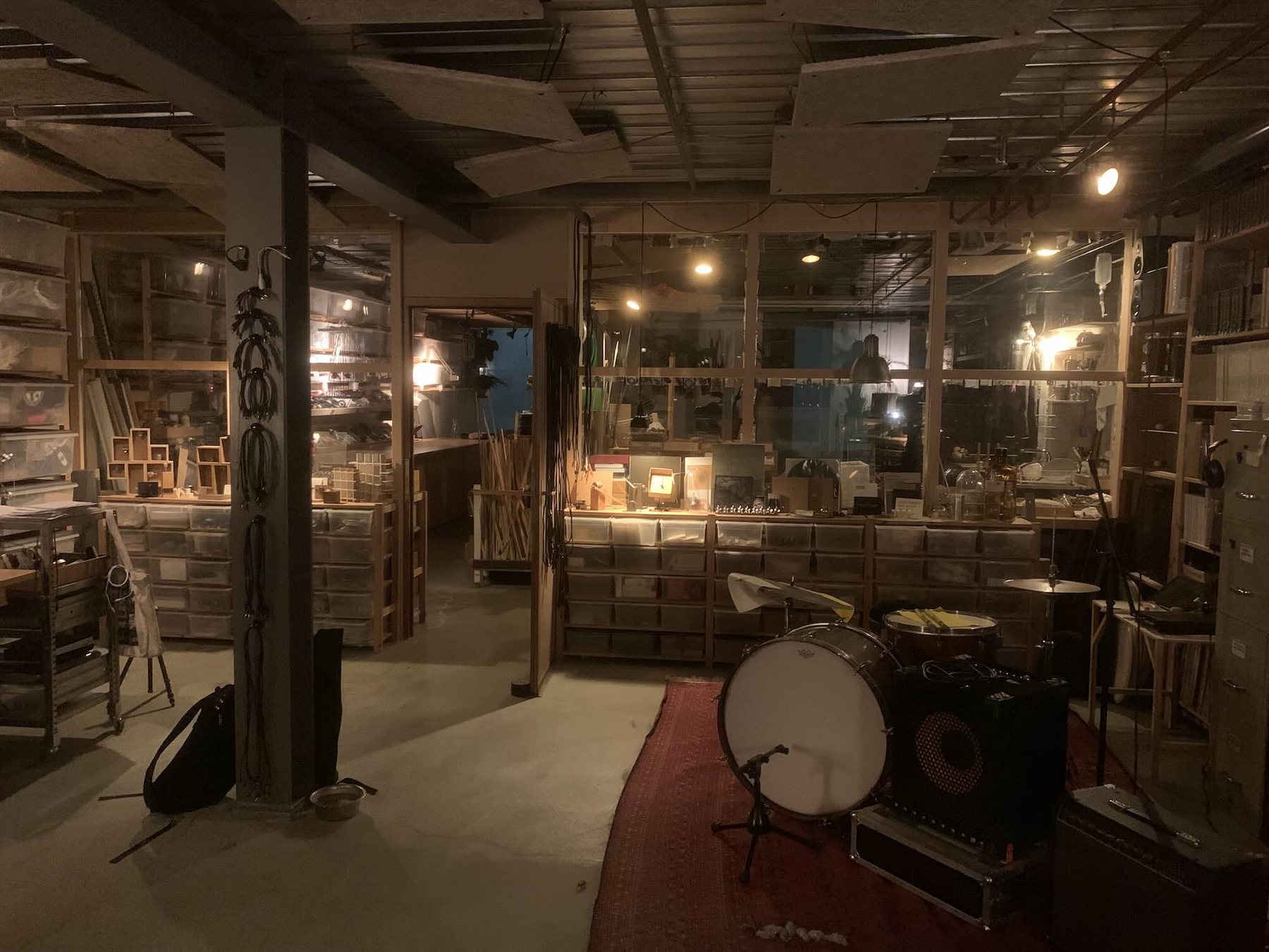 A workshop room adjoining the studio, shelves of small wooden and metal components, a drum kit in the foreground.