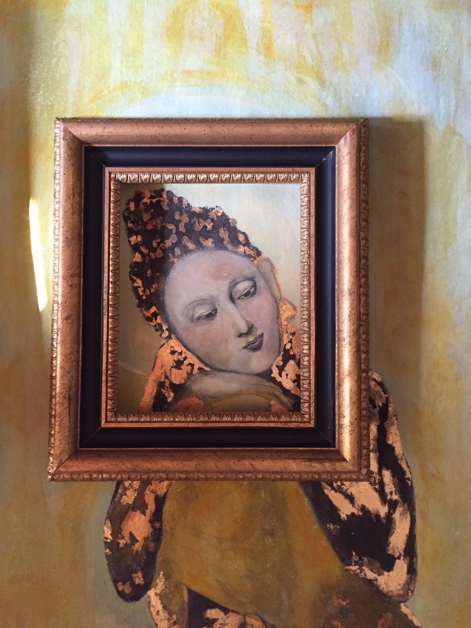 A finished painting of a seated figure with a pale halo, gold leaf patterning the robe, on a soft green ground.