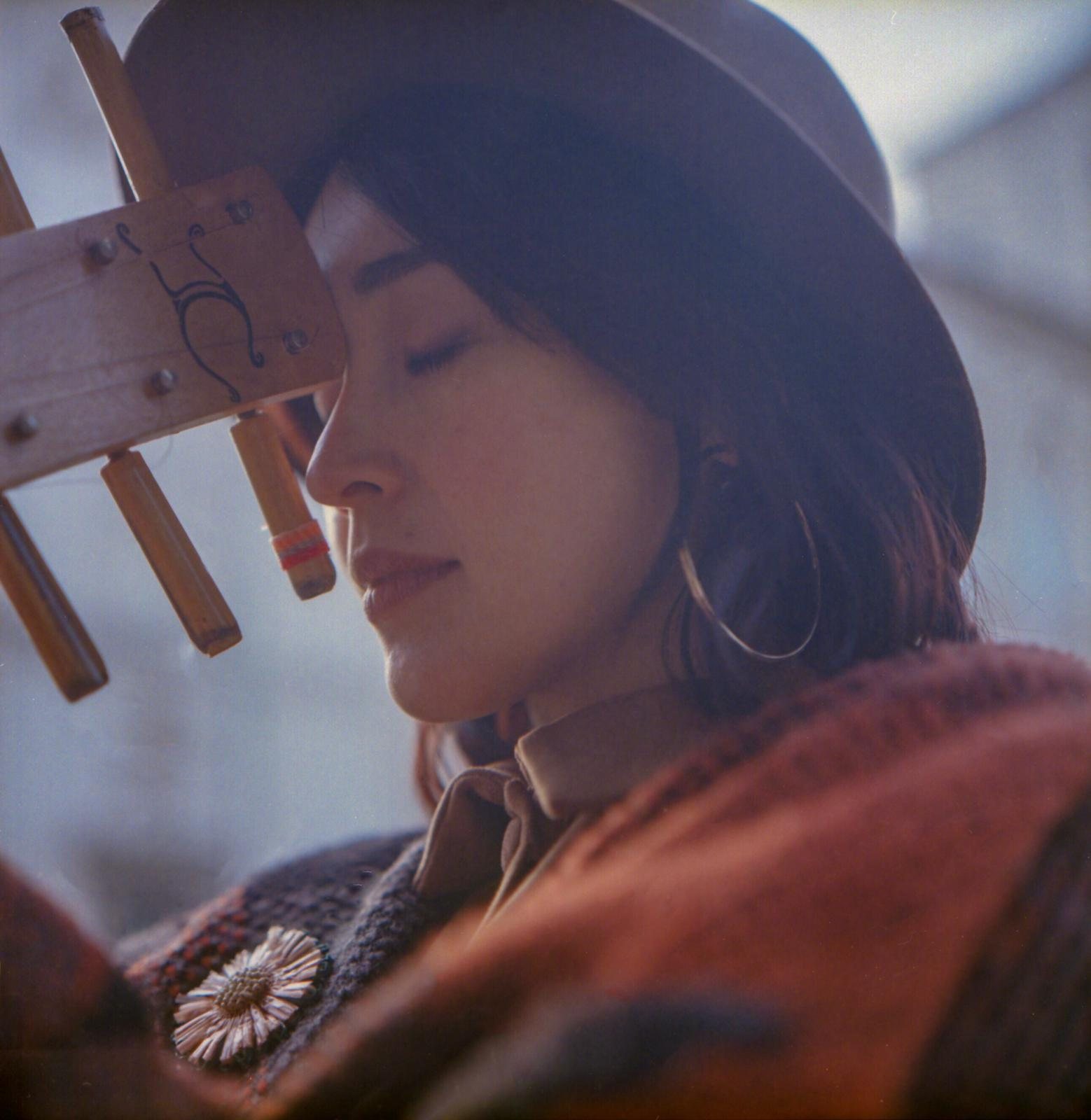 Colour film photograph of Jacelyn with eyes closed, the headstock of the sape pressed gently against her forehead, side profile, warm winter light.
