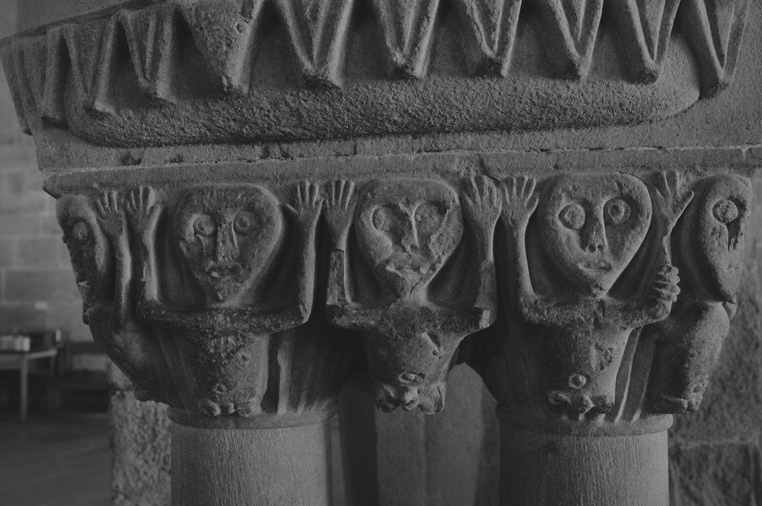 A carved Romanesque capital showing rows of stylised figures with raised hands, worn stone.