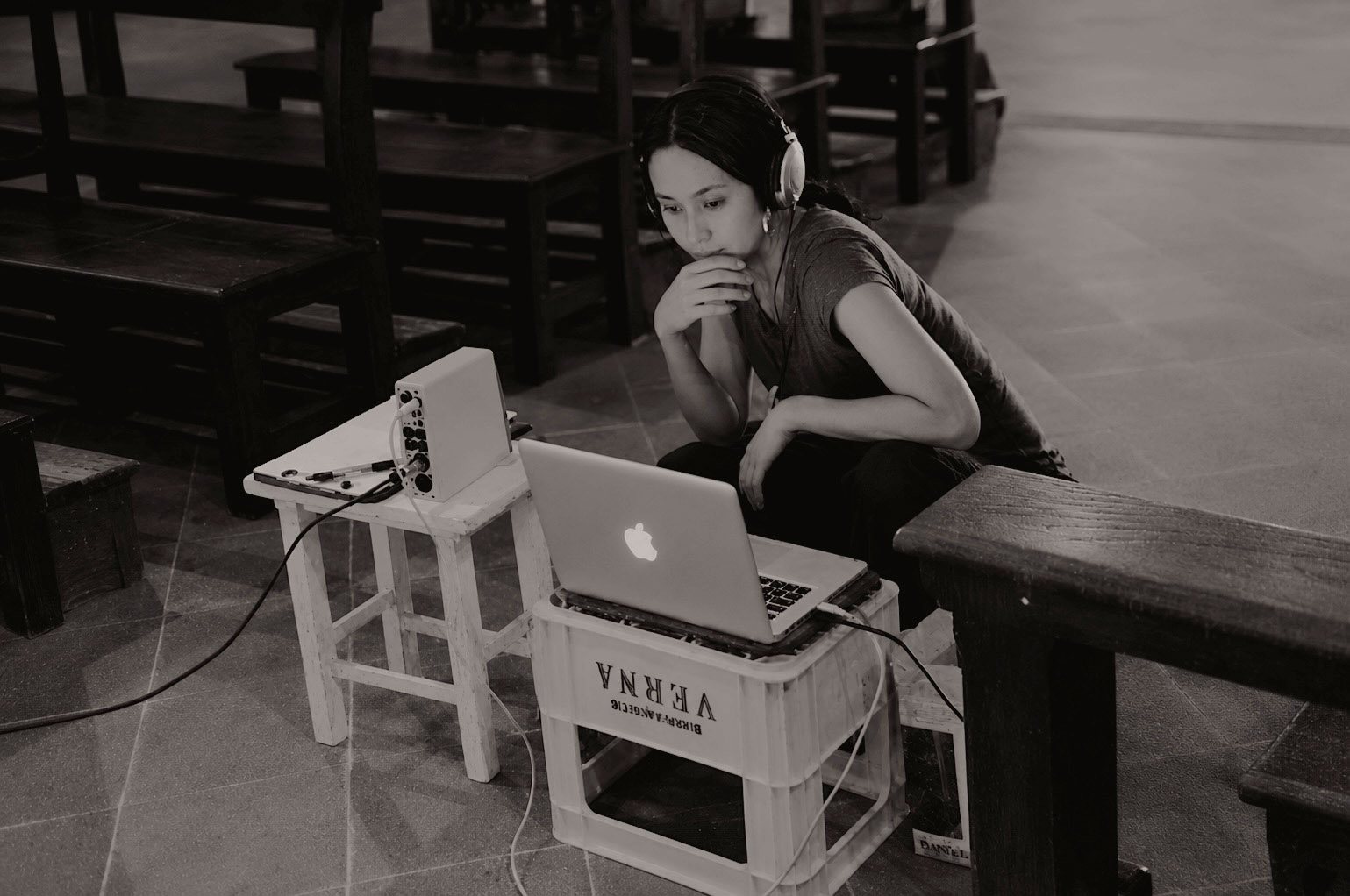 A MacBook resting on an upturned plastic crate beside recording equipment, inside the church.