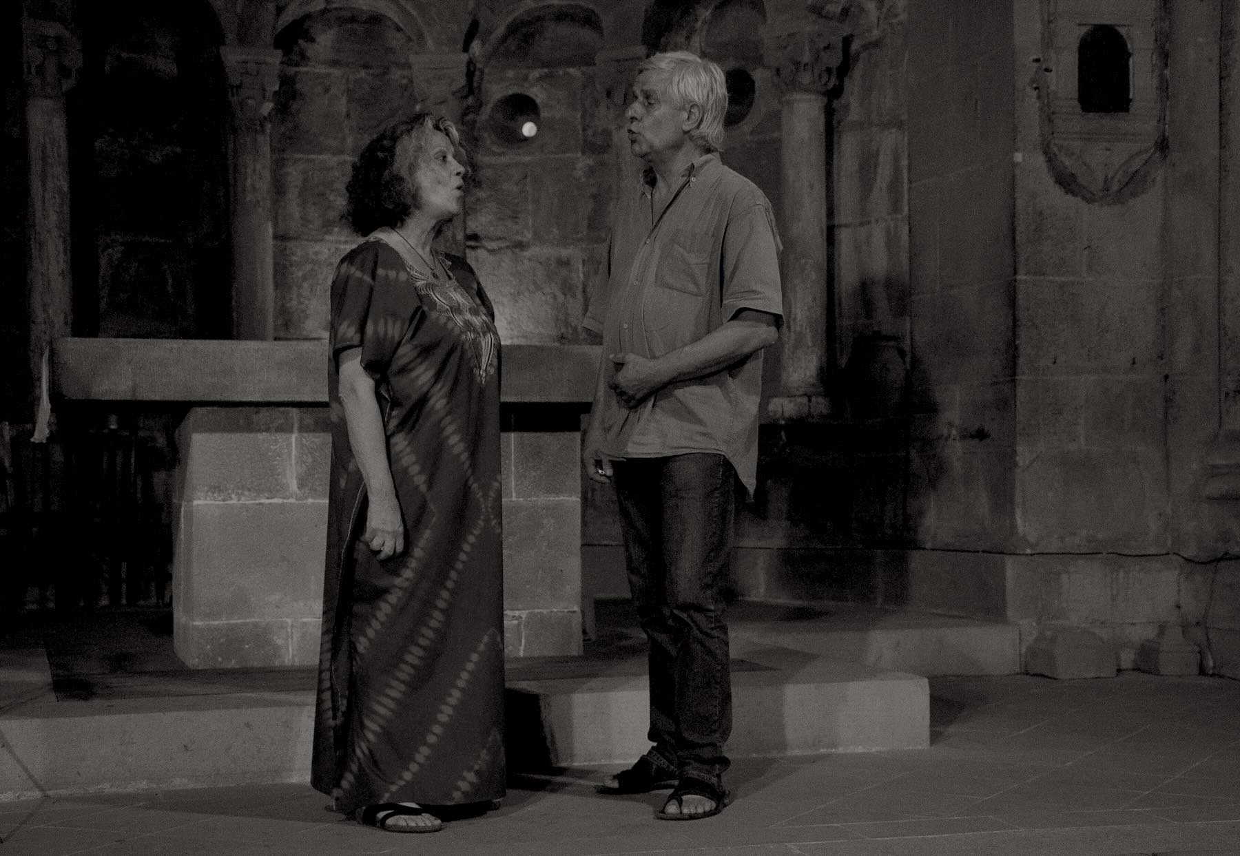 Two singers facing each other mid-performance inside the Romanesque apse, dressed simply, mid-phrase.